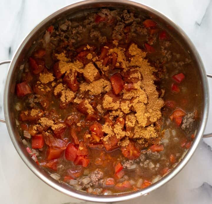 Diced tomatoes, beef broth and taco seasoning being added to the cooked beef, onions and peppers in a largo pot.